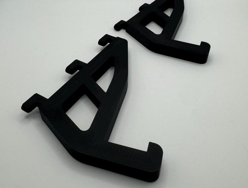 May include: Two black plastic shelf brackets with a grid pattern. The brackets are designed to support shelves.