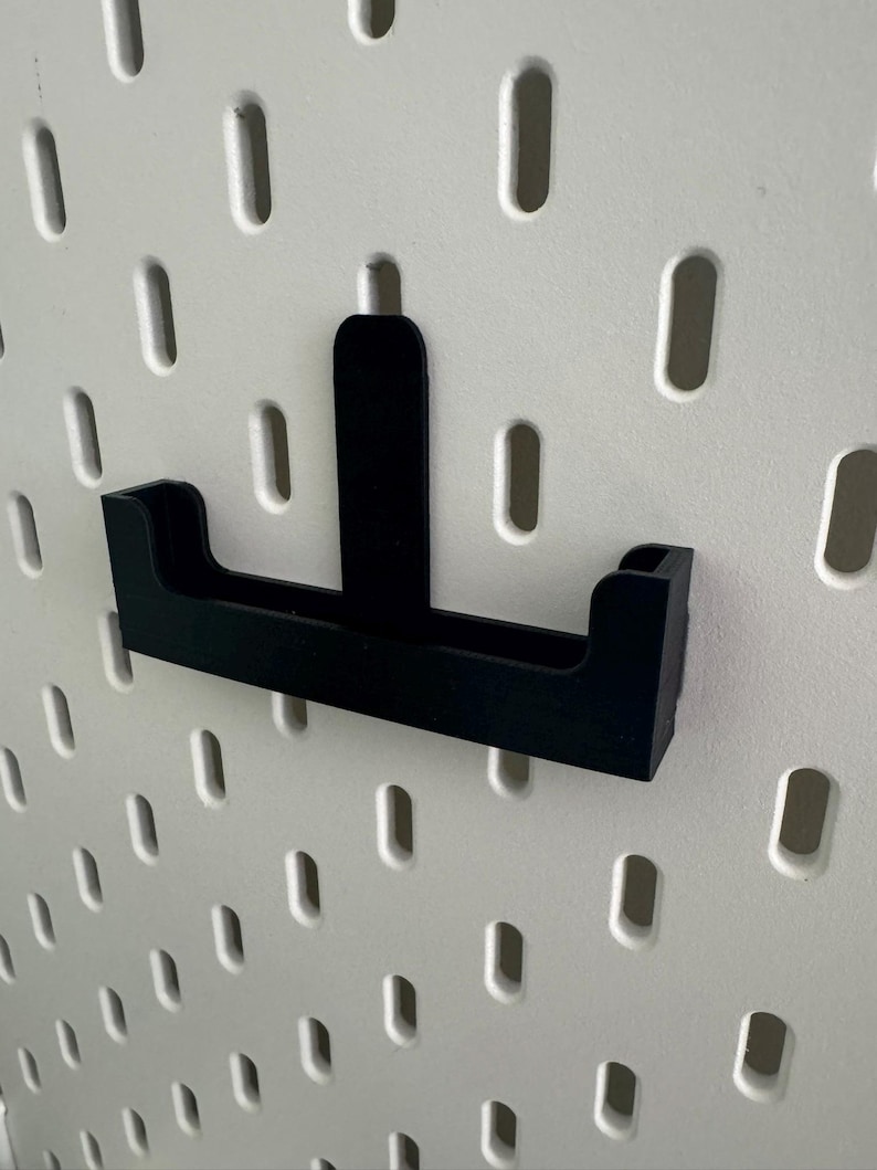 May include: Black plastic pegboard hook with a small shelf. The hook is designed to hold small items like tools or accessories.