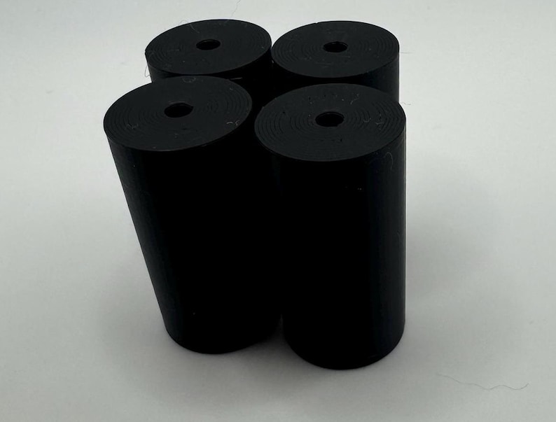 May include: Four black cylindrical objects with a hole in the center. The objects are arranged in a square shape.