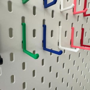 May include: A pegboard with various colored hooks. The hooks are in the shape of an L and are made of plastic. The colors of the hooks are black, green, blue, white, pink, and red.