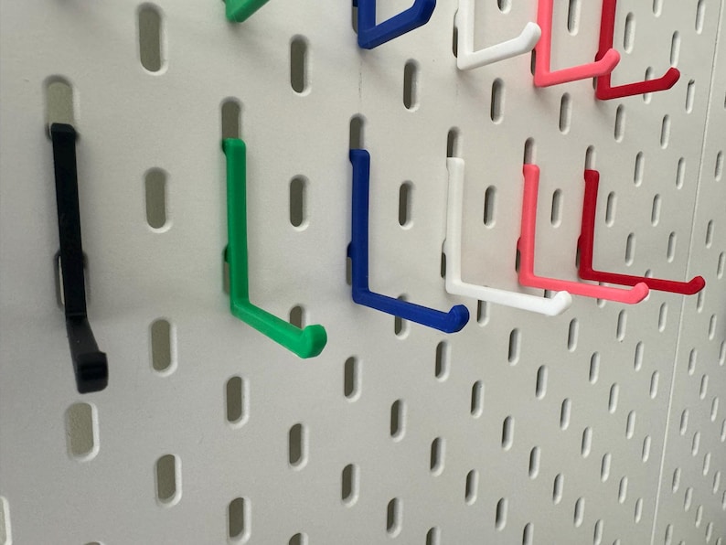 May include: A pegboard with various colored hooks. The hooks are in the shape of an L and are made of plastic. The colors of the hooks are black, green, blue, white, pink, and red.