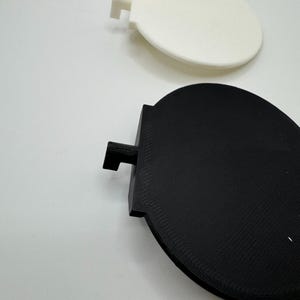 Op de afbeelding: Twee ronde, 3D-geprinte schijven, een witte en een zwarte, met een klein lipje aan de zijkant van elke schijf.