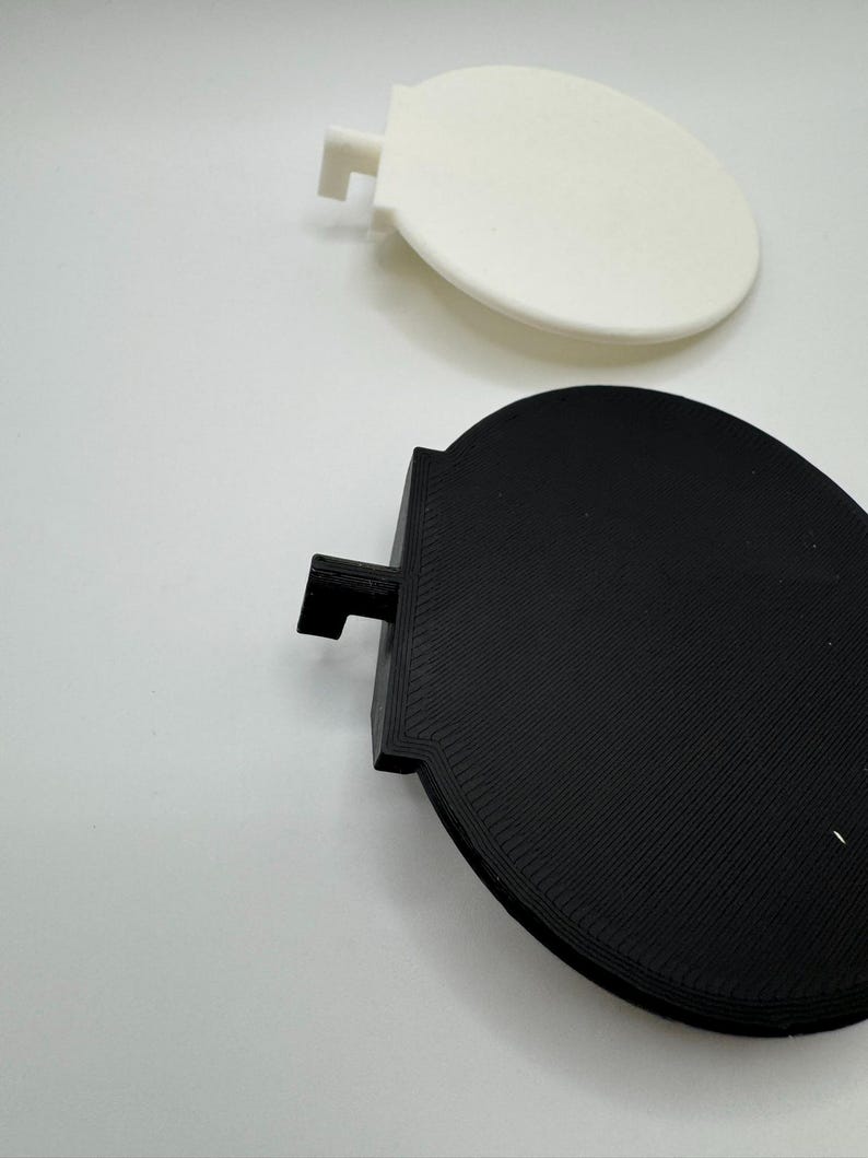 Op de afbeelding: Twee ronde, 3D-geprinte schijven, een witte en een zwarte, met een klein lipje aan de zijkant van elke schijf.