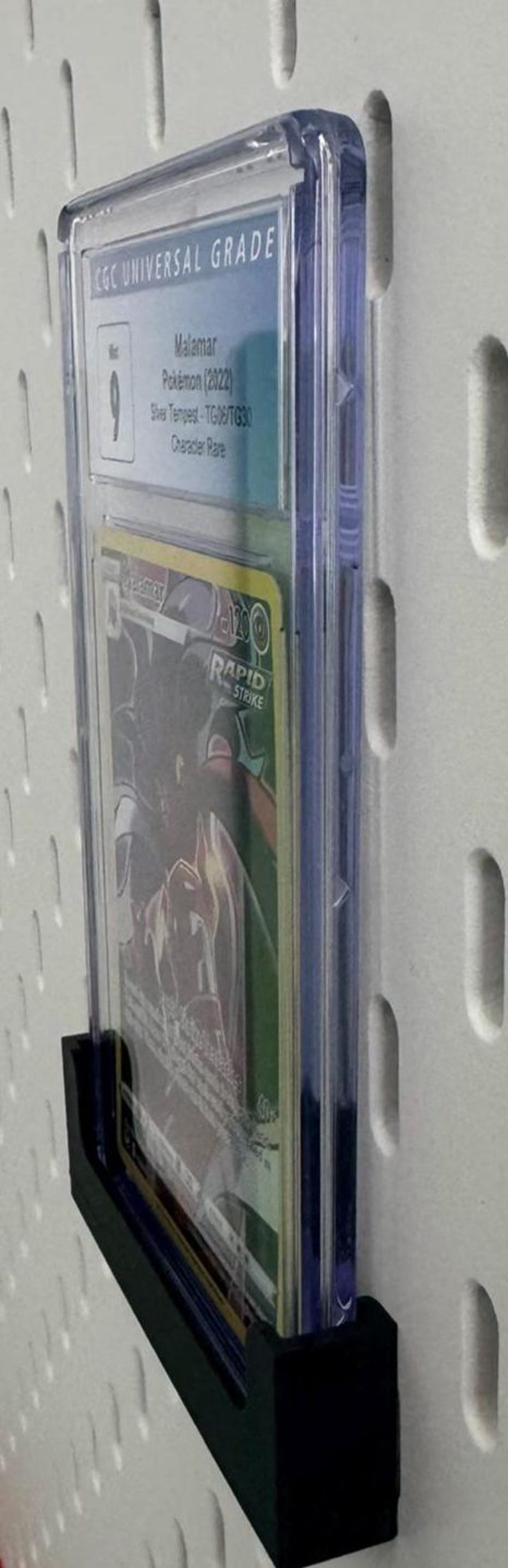 May include: A clear plastic graded card case with a black card holder. The card case has a label that reads "CGC UNIVERSAL GRADE" and a number "9". The card inside the case is a Pokemon card featuring the character "Malamar" from the "Silver Tempest" set. The card is a "Character Rare" card.
