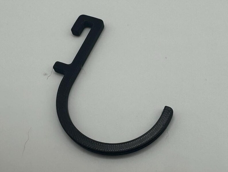 Puede incluir: Un gancho de pl&aacute;stico negro con un extremo redondeado. El gancho est&aacute; dise&ntilde;ado para colgar objetos en una pared o puerta.