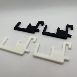 Puede incluir: Cuatro formas geom&eacute;tricas de pl&aacute;stico, en blanco y negro. Dos son negras y dos son blancas. Cada una tiene una base rectangular con una extensi&oacute;n en forma de gancho y una proyecci&oacute;n rectangular m&aacute;s peque&ntilde;a.