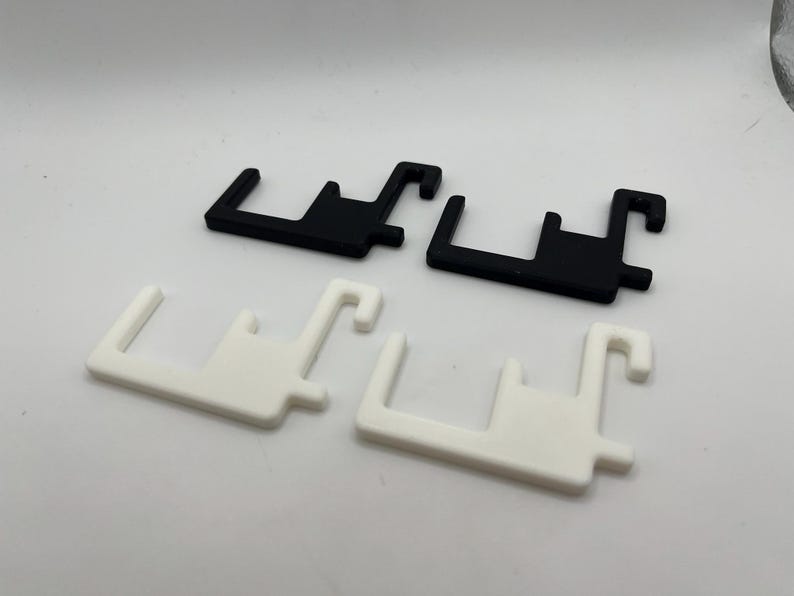 Puede incluir: Cuatro formas geom&eacute;tricas de pl&aacute;stico, en blanco y negro. Dos son negras y dos son blancas. Cada una tiene una base rectangular con una extensi&oacute;n en forma de gancho y una proyecci&oacute;n rectangular m&aacute;s peque&ntilde;a.