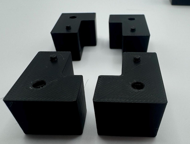 May include: Four black plastic corner brackets with a square shape and a small hole in the centre of each side.