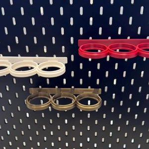 May include: Three wall-mounted cup holders in different colors: white, red, and brown. Each holder has three circular openings for cups.