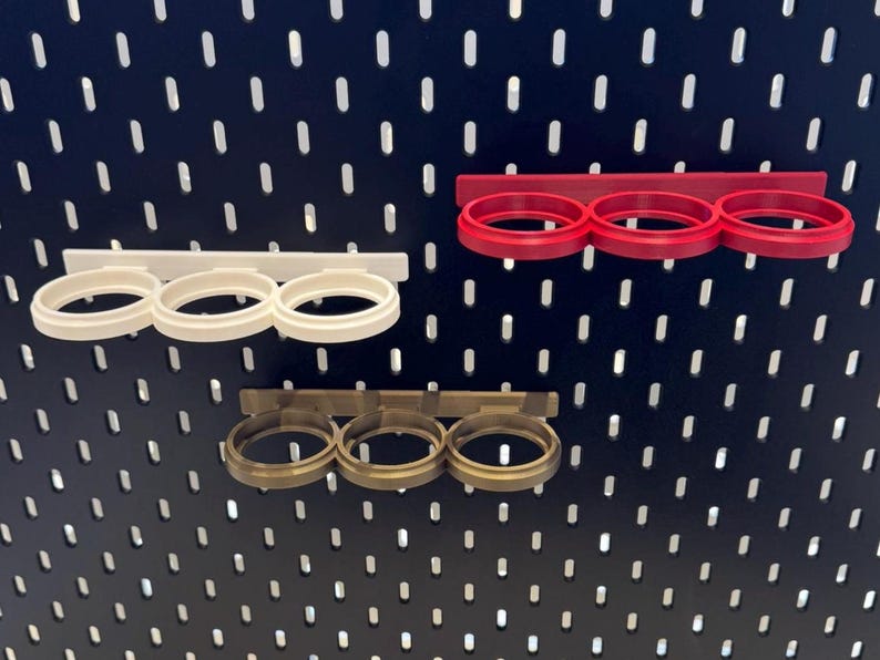 May include: Three wall-mounted cup holders in different colors: white, red, and brown. Each holder has three circular openings for cups.