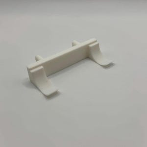Op de afbeelding: Wit plastic model auto-onderdeel met twee gebogen vleugels aan elke kant. Het onderdeel is ontworpen om aan de achterkant van een model auto te worden bevestigd.