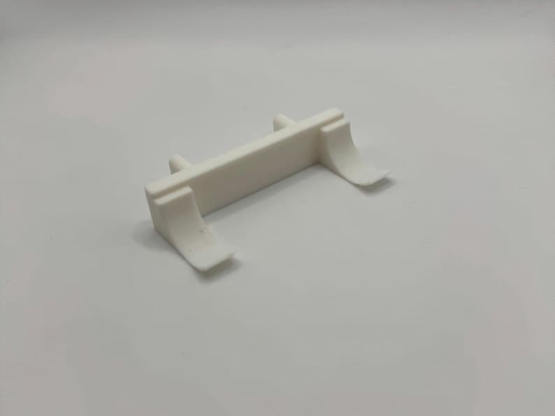 Op de afbeelding: Wit plastic model auto-onderdeel met twee gebogen vleugels aan elke kant. Het onderdeel is ontworpen om aan de achterkant van een model auto te worden bevestigd.