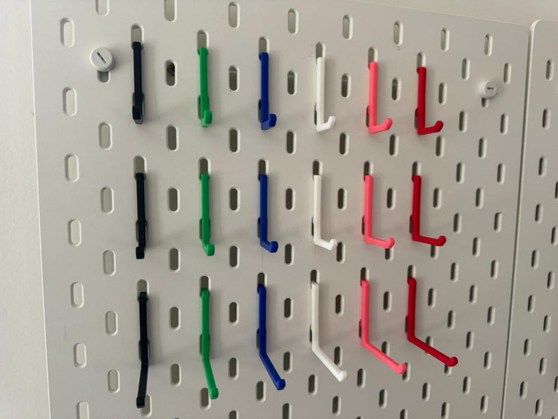 May include: A pegboard with hooks in various colors, including black, green, blue, white, pink, and red. The hooks are arranged in rows and columns on the pegboard.