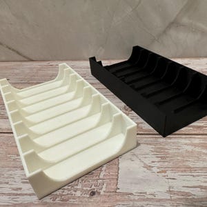 K&ouml;nnte beinhalten: Zwei rechteckige Organizer, einer wei&szlig; und einer schwarz, nebeneinander. Jeder Organizer hat gebogene Trennw&auml;nde, die einzelne F&auml;cher bilden. Die Organizer bestehen aus einem glatten Material und stehen auf einer Holzoberfl&auml;che.