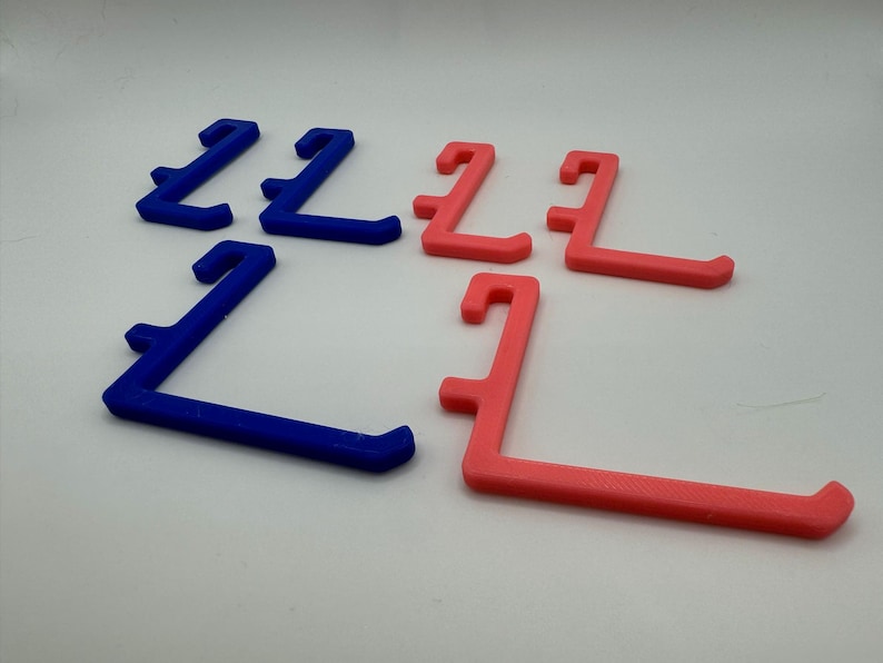 May include: A set of six plastic hooks, three blue and three pink, designed for hanging items. The hooks are shaped like an L and have a rounded edge.