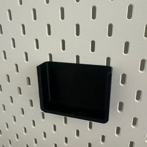 Op de afbeelding: Een zwart plastic pegboard-plank met een witte achtergrond.