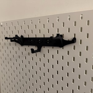 May include: A black pegboard organizer with multiple hooks and a unique design. The organizer is mounted on a white pegboard, providing a functional and stylish storage solution for various items.