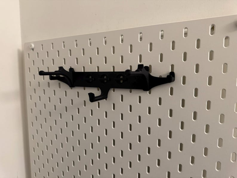 May include: A black pegboard organizer with multiple hooks and a unique design. The organizer is mounted on a white pegboard, providing a functional and stylish storage solution for various items.