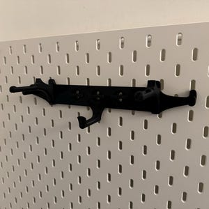 May include: Black pegboard organizer with multiple hooks and a unique design. The organizer is mounted on a white pegboard, providing a stylish storage solution. Perfect for organizing tools, accessories, or other items.