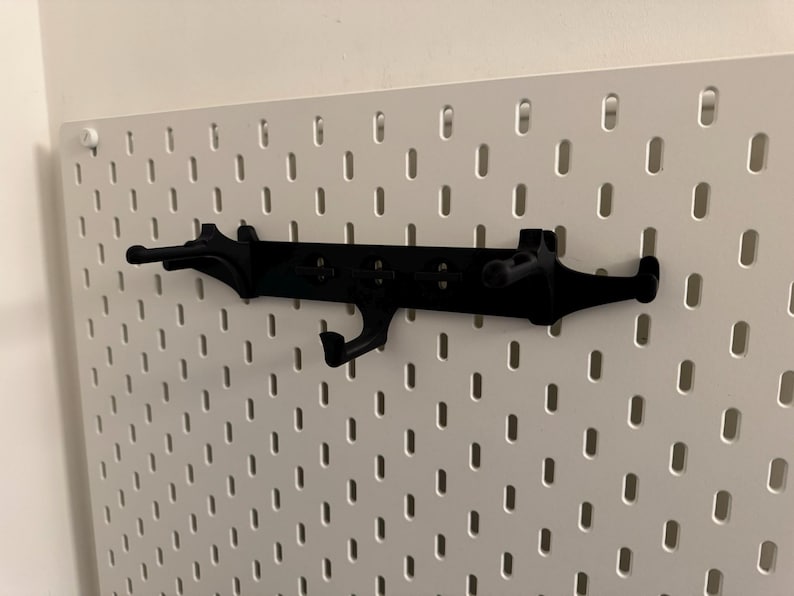 May include: Black pegboard organizer with multiple hooks and a unique design. The organizer is mounted on a white pegboard, providing a stylish storage solution. Perfect for organizing tools, accessories, or other items.