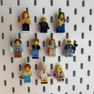 K&ouml;nnte beinhalten: Elf Lego-Minifiguren mit unterschiedlichen Outfits und Accessoires, pr&auml;sentiert auf einer wei&szlig;en Lochwand. Die Figuren repr&auml;sentieren verschiedene Berufe und Stile, darunter ein Polizist, ein Koch und eine Gesch&auml;ftsfrau. Der Hintergrund ist eine wei&szlig;e Lochwand.