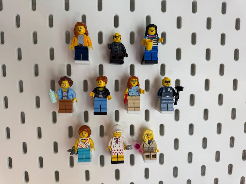 K&ouml;nnte beinhalten: Elf Lego-Minifiguren mit unterschiedlichen Outfits und Accessoires, pr&auml;sentiert auf einer wei&szlig;en Lochwand. Die Figuren repr&auml;sentieren verschiedene Berufe und Stile, darunter ein Polizist, ein Koch und eine Gesch&auml;ftsfrau. Der Hintergrund ist eine wei&szlig;e Lochwand.