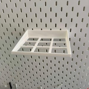 Op de afbeelding: Wit plasticen plank met een rasterpatroon, gemonteerd op een witte prikbordwand.