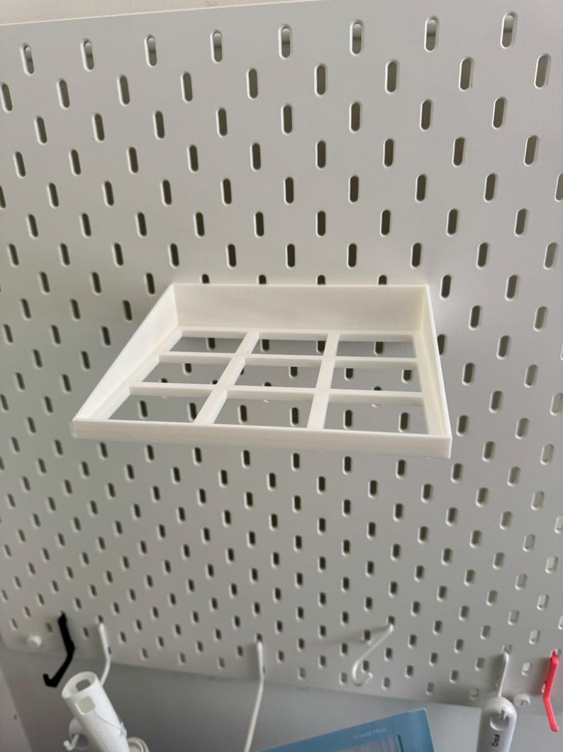 Op de afbeelding: Wit plasticen plank met een rasterpatroon, gemonteerd op een witte prikbordwand.
