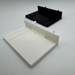 May include: A white plastic shelf with a black plastic shelf behind it. Both shelves have a raised lip on the front edge.