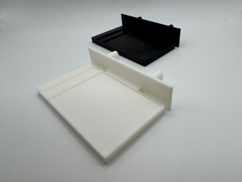 May include: A white plastic shelf with a black plastic shelf behind it. Both shelves have a raised lip on the front edge.
