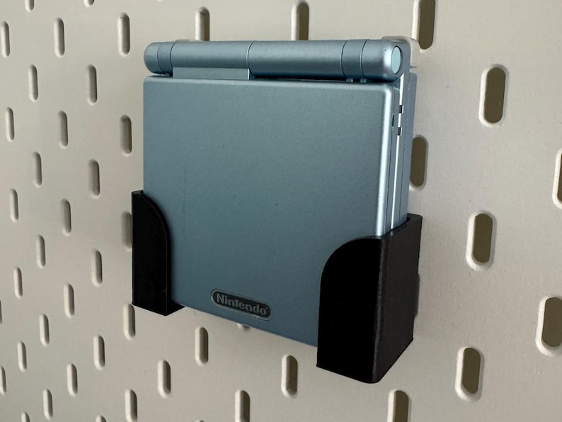 Pu&ograve; includere: Una console per videogiochi portatile Game Boy Advance SP blu con un supporto da parete nero. La console ha il logo Nintendo sul davanti.