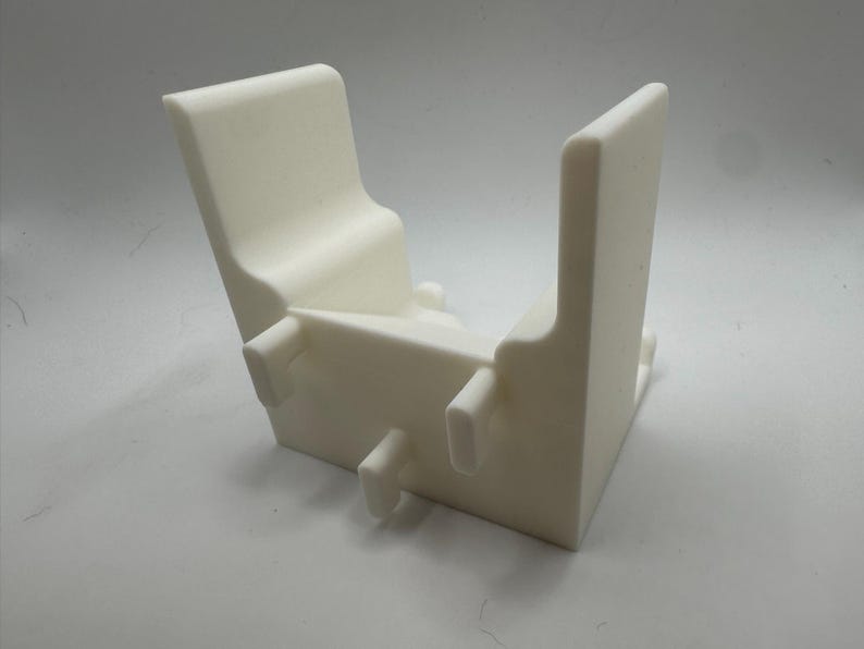 K&ouml;nnte beinhalten: Ein wei&szlig;es, eckiges, 3D-gedrucktes Objekt mit U-f&ouml;rmigem Design. Es hat zwei aufrechte, rechteckige Seiten, die durch eine Basis mit drei kleinen, zylindrischen Vorspr&uuml;ngen verbunden sind. Das Objekt hat eine glatte, matte Oberfl&auml;che und scheint aus Kunststoff zu sein.