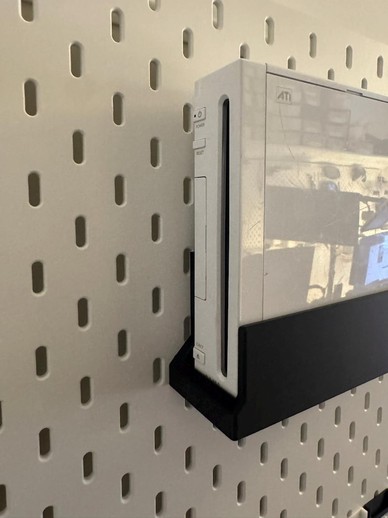 Peut inclure: Une console de jeu blanche mont&eacute;e sur un panneau perfor&eacute; blanc avec un support noir. La console porte le mot "ATI". Le panneau perfor&eacute; pr&eacute;sente des trous ovales espac&eacute;s uniform&eacute;ment.
