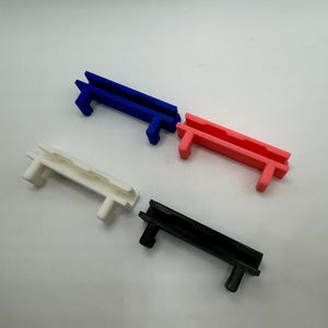Pode incluir: Quatro clipes de cabo de pl&aacute;stico em diferentes cores: azul, rosa, branco e preto. Os clipes s&atilde;o projetados para segurar os cabos no lugar.
