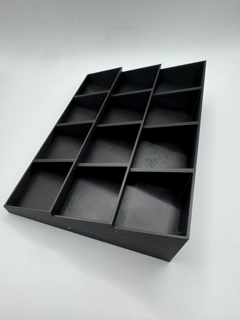 Peut inclure: Un organisateur noir inclin&eacute; avec plusieurs compartiments rectangulaires. L'organisateur est fait d'un mat&eacute;riau solide et est con&ccedil;u pour contenir de petits objets. Les compartiments sont dispos&eacute;s en gradins.