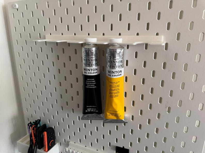 May include: Two tubes of Winton Oil Colour paint, one black and one yellow, displayed on a white pegboard. The black tube is labeled "Lamp Black" and the yellow tube is labeled "Lemon Yellow". Each tube is 200 ml or 6.76 US fl oz.
