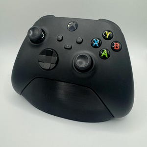 May include: A black Xbox controller with a textured surface. The controller has a black and white d-pad, a black analog stick, and black buttons with colored labels: Y, X, A, and B.