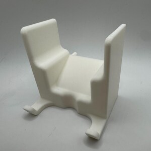 K&ouml;nnte beinhalten: Ein wei&szlig;es, 3D-gedrucktes Objekt in Wiegenform. Es hat eine rechteckige Basis mit zwei gebogenen F&uuml;&szlig;en, eine zentrale Plattform und zwei aufrechte St&uuml;tzen. Das Design ist minimalistisch und modern, mit glatten, abgerundeten Kanten.
