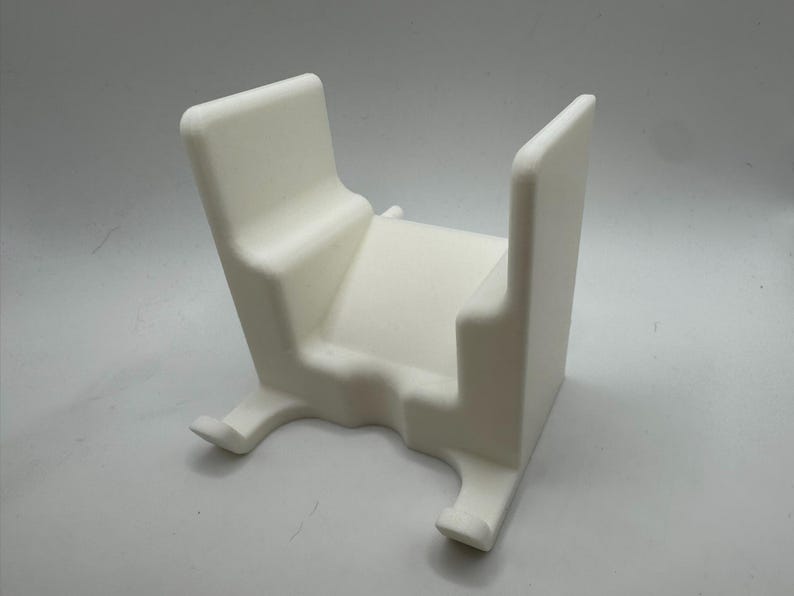 K&ouml;nnte beinhalten: Ein wei&szlig;es, 3D-gedrucktes Objekt in Wiegenform. Es hat eine rechteckige Basis mit zwei gebogenen F&uuml;&szlig;en, eine zentrale Plattform und zwei aufrechte St&uuml;tzen. Das Design ist minimalistisch und modern, mit glatten, abgerundeten Kanten.