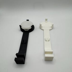 K&ouml;nnte beinhalten: Zwei 3D-gedruckte Handyst&auml;nder, einer schwarz und einer wei&szlig;. Beide St&auml;nder haben eine runde Basis und einen langen, geraden Arm mit einem rechteckigen Handyhalter am Ende.