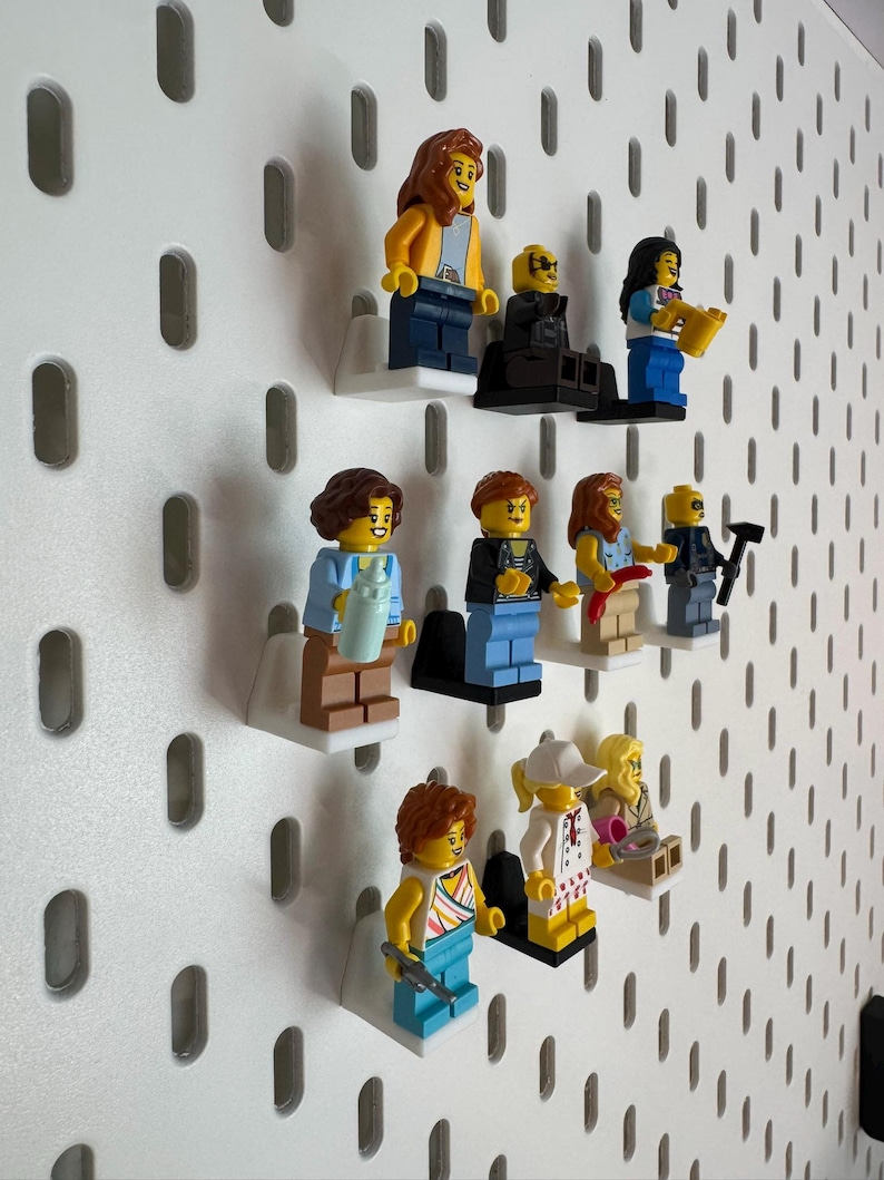 K&ouml;nnte beinhalten: Eine Sammlung von Lego-Minifiguren, die auf einer wei&szlig;en Lochwand ausgestellt sind. Die Minifiguren tragen verschiedene Outfits und Accessoires, darunter Werkzeuge, Getr&auml;nke und Musikinstrumente. Die Figuren sind auf kleinen wei&szlig;en Regalen montiert.
