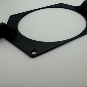 以下が含まれることがあります： 4つの取り付け穴のある黒いプラスチック製のファンマウント。マウントには、ファン用の円形の切り抜きがあります。