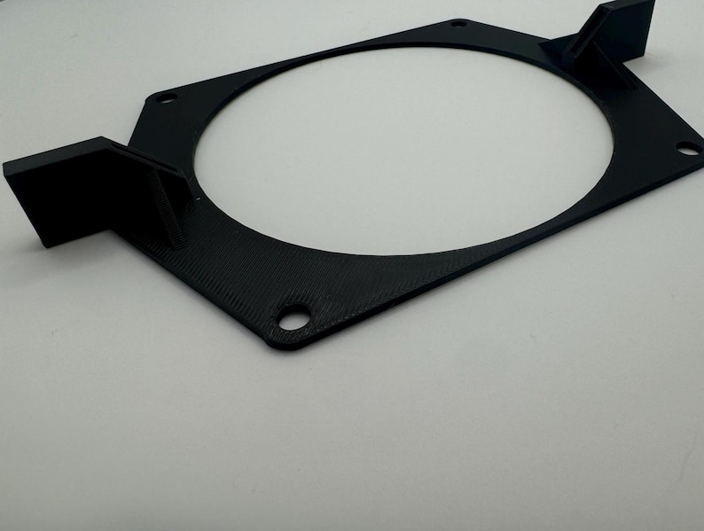 以下が含まれることがあります： 4つの取り付け穴のある黒いプラスチック製のファンマウント。マウントには、ファン用の円形の切り抜きがあります。
