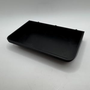 Puede incluir: Una bandeja rectangular de pl&aacute;stico negro con bordes ligeramente redondeados. La bandeja tiene tres peque&ntilde;os agujeros en el borde superior.