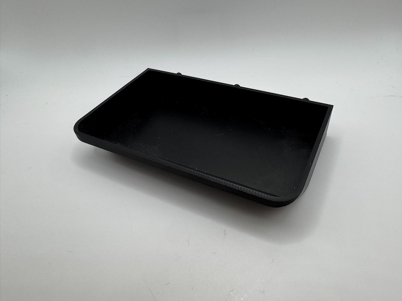 Puede incluir: Una bandeja rectangular de pl&aacute;stico negro con bordes ligeramente redondeados. La bandeja tiene tres peque&ntilde;os agujeros en el borde superior.