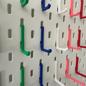 May include: A pegboard with various colored hooks. The hooks are in the shape of an L and are made of plastic. The colors of the hooks are black, green, blue, white, pink, and red.