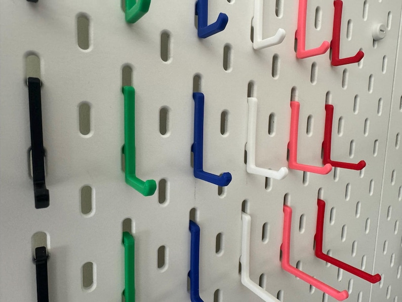 May include: A pegboard with various colored hooks. The hooks are in the shape of an L and are made of plastic. The colors of the hooks are black, green, blue, white, pink, and red.