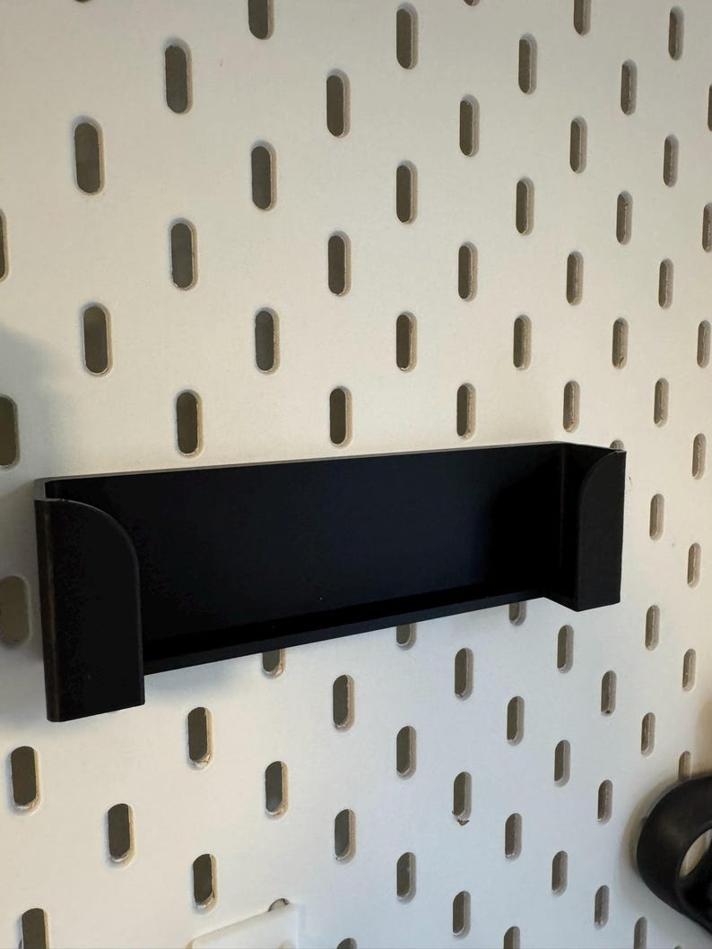 Puede incluir: Un estante negro con lados curvos est&aacute; montado en una pared perforada blanca. El estante es rectangular con una base plana y est&aacute; dise&ntilde;ado para sostener objetos. La pared perforada tiene agujeros ovalados espaciados.