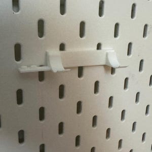 May include: White plastic pegboard with a white plastic hook attached to it.