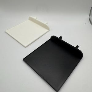 Pode incluir: Duas bandejas quadradas impressas em 3D, uma branca e outra preta. As bandejas t&ecirc;m uma borda elevada ao redor da borda e duas pequenas sali&ecirc;ncias na parte de tr&aacute;s.